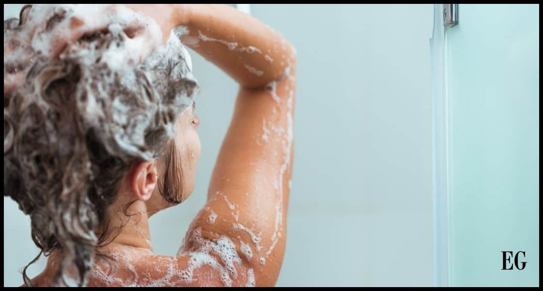 Mujer lavándose el cabello rizado con champú en la ducha.