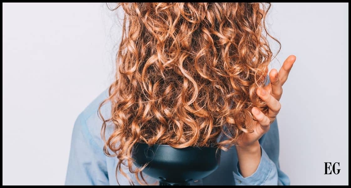 Mujer de espaldas secando su cabello rizado con un difusor de mano